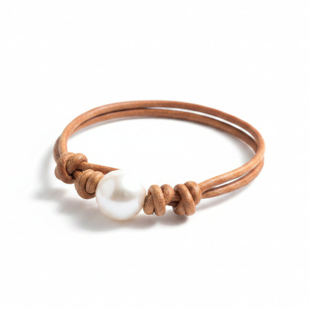 Bracelet with a white bead and brown leather strap on a textured stone surface near water.