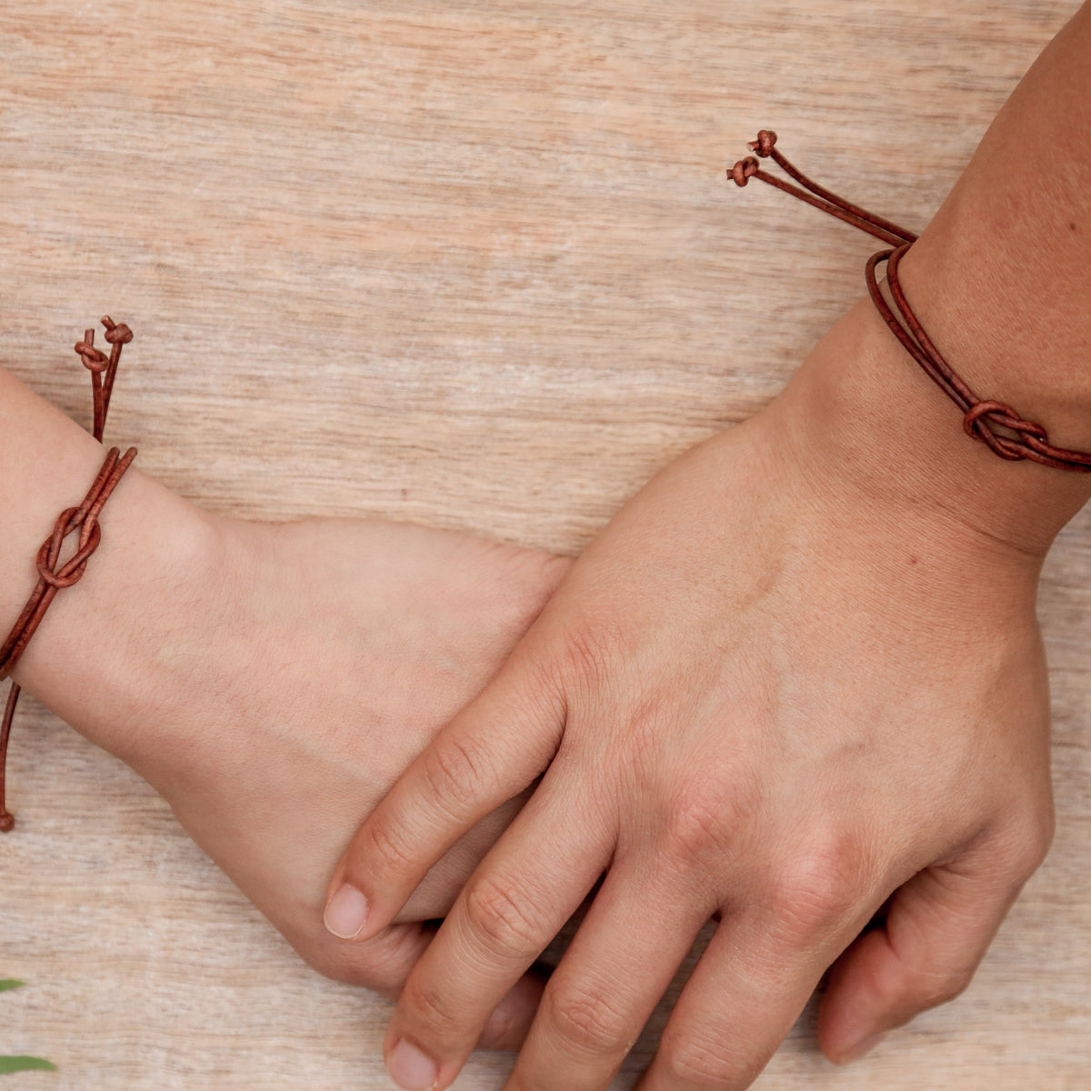 Two wrists with brown bracelets on a wooden surface
