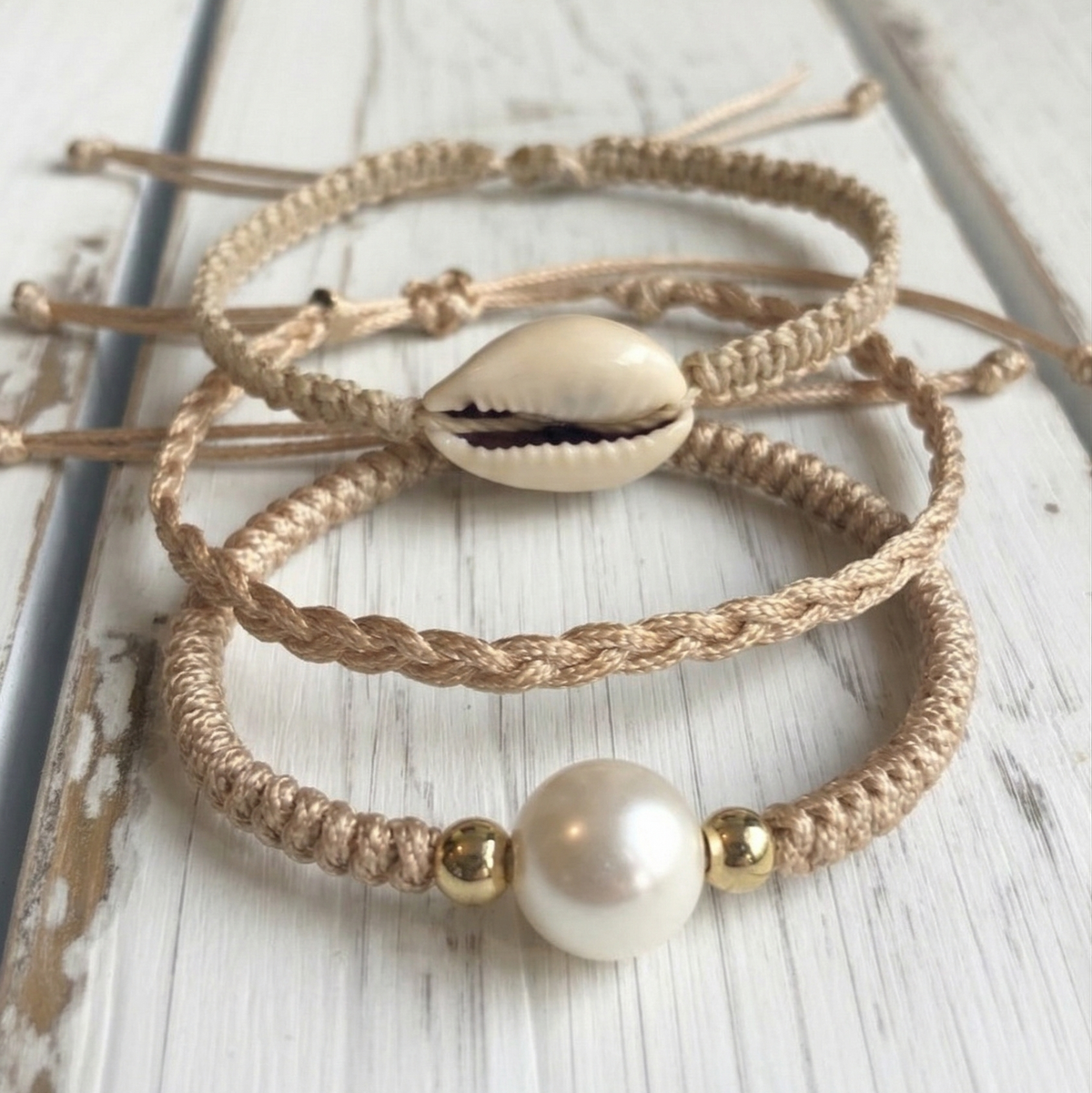 Three braided bracelets with shell and pearl beads on a wooden surface