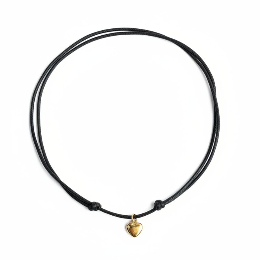 Black cord necklace with a gold heart charm on a white surface