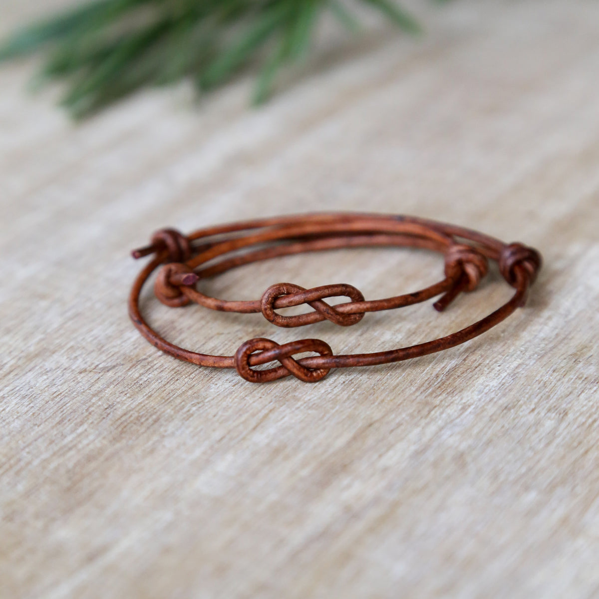 Two brown leather bracelets with knot designs on a light wooden surface.