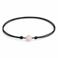 Rose quartz stone bead choker on black waxed cord with adjustable slide-knot closure, laid on a rustic wooden background.