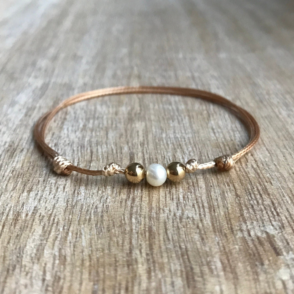 Gold cord bracelet with a single white pearl bead and two gold beads.