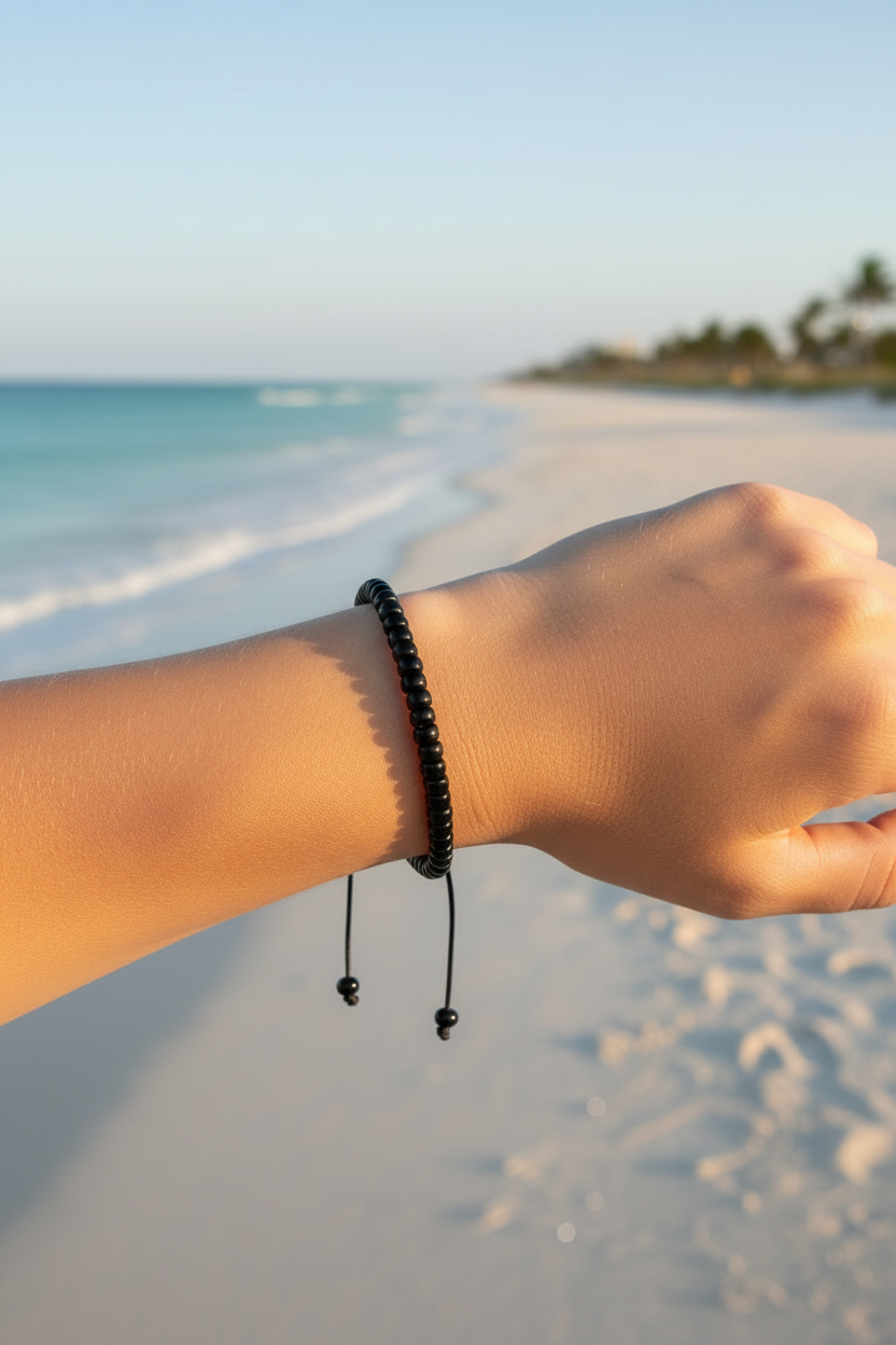 Hand wearing a black beaded bracelet on a beach with ocean and sky in the background