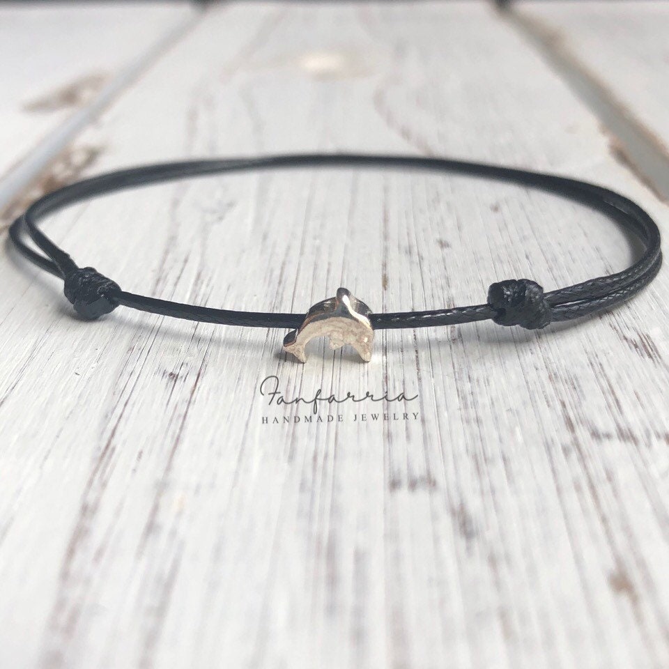 A black cord anklet bracelet featuring a sterling silver dolphin charm. The bracelet has a minimalist design.