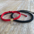 Matching red and black couple bracelets with gold heart charm on wood background