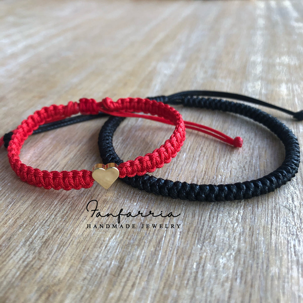 Matching red and black couple bracelets with gold heart charm on wood background
