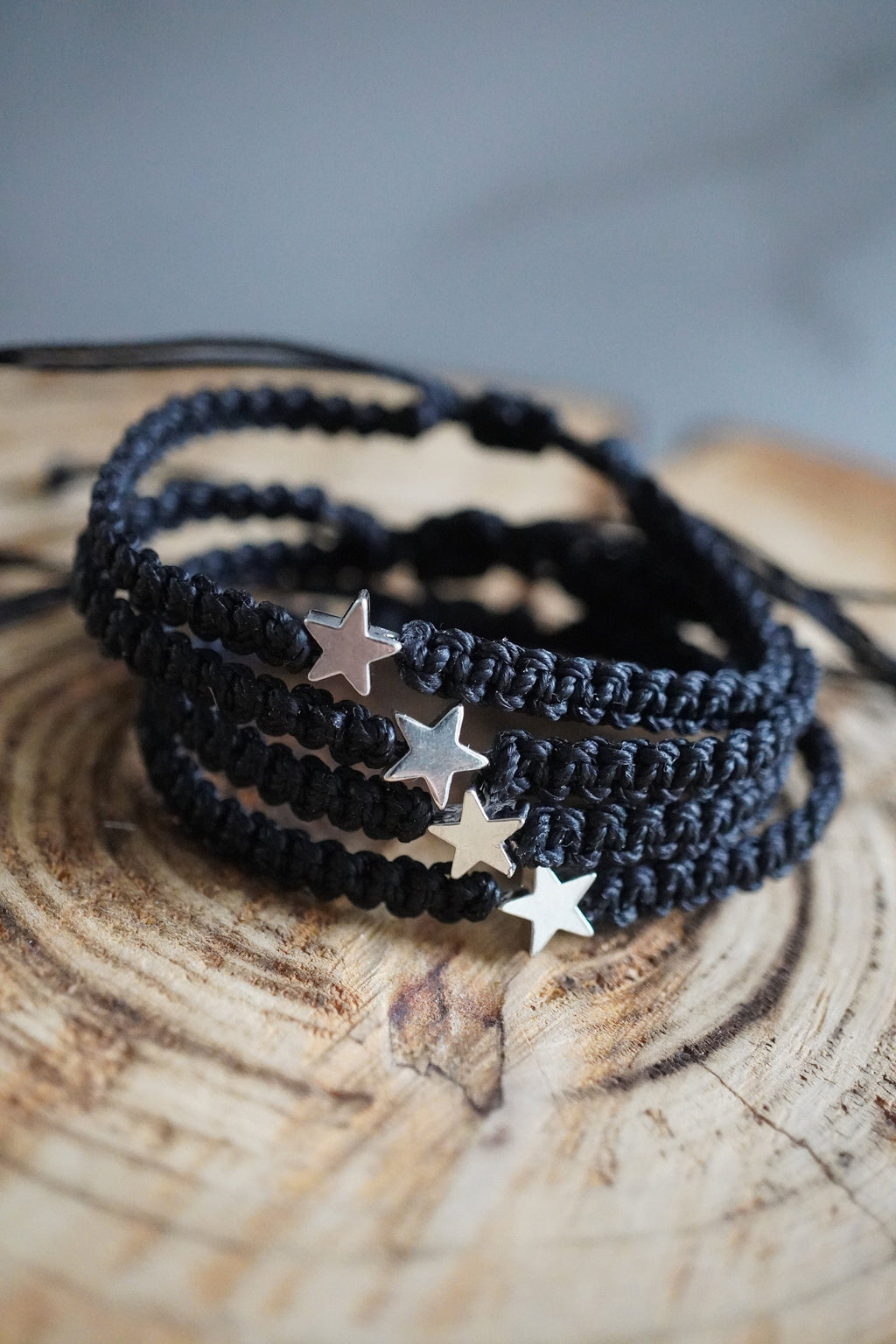 May include: Four black braided matching bracelets with silver star charms. The bracelets are stacked on top of each other.