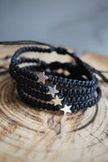 May include: Four black braided matching bracelets with silver star charms. The bracelets are stacked on top of each other.