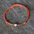 A simple orange string anklet bracelet with a small gold heart charm.