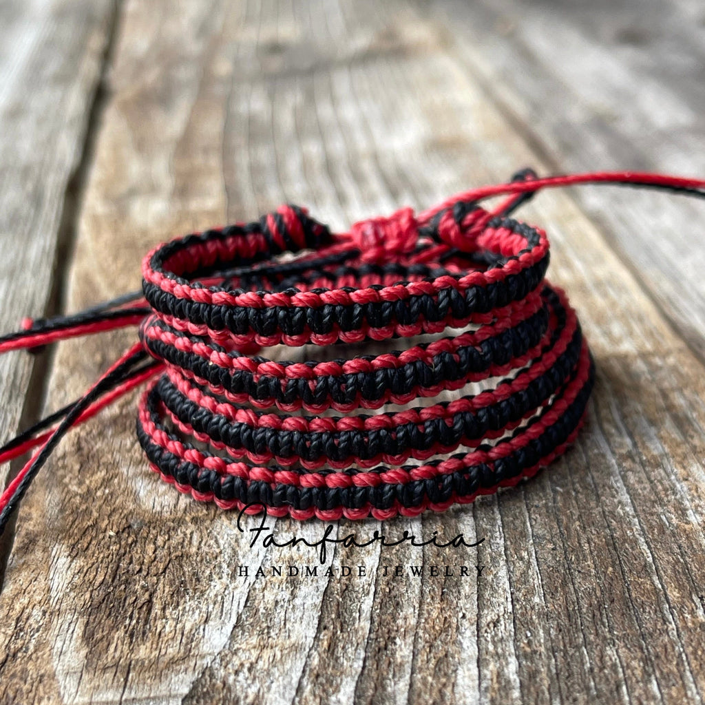 Red and black matching friendship bracelets stacked on top of each other. The bracelets are made of woven string and are tied together with a knot. The bracelets are on a wooden surface.