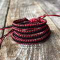 Red and black matching friendship bracelets stacked on top of each other. The bracelets are made of woven string and are tied together with a knot. The bracelets are on a wooden surface.