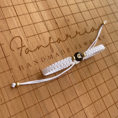 Handmade white macrame bracelet with a black enamel letter bead and gold accents. The bracelet is adjustable with a sliding knot closure.