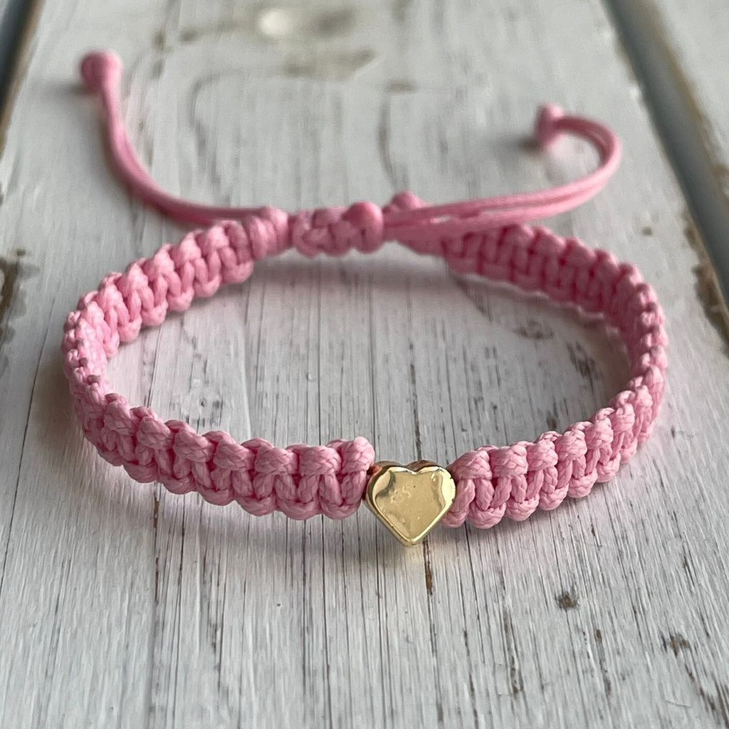 A pink braided bracelet with a gold heart charm.