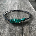 Boho chic bracelet or anklet with black adjustable cord and green malachite chips, displayed on a rustic wooden surface. The piece features a natural stone design, perfect for a beach or festival look.