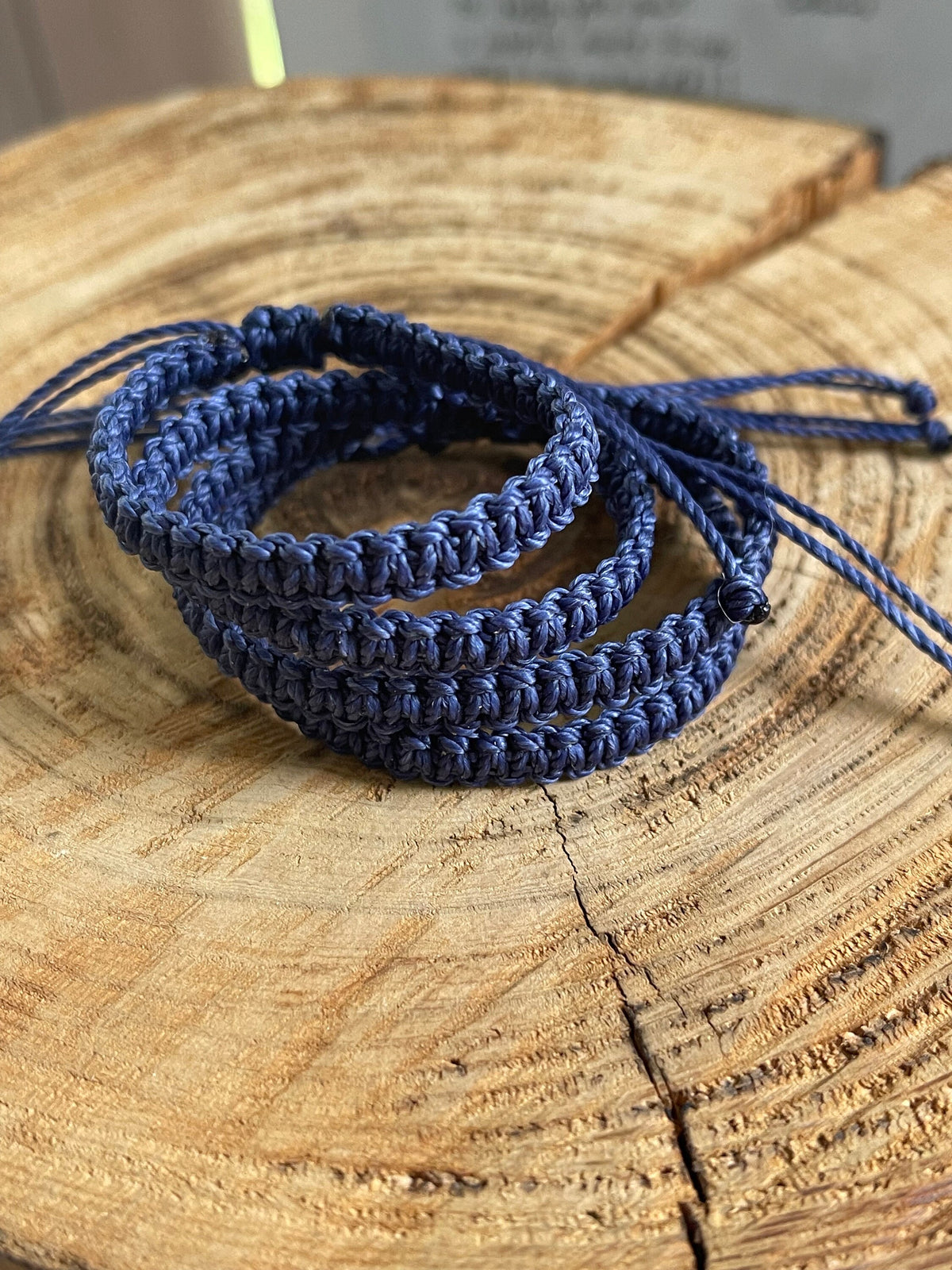 May include: Three blue braided friendship bracelets with black beads on a wooden surface.
