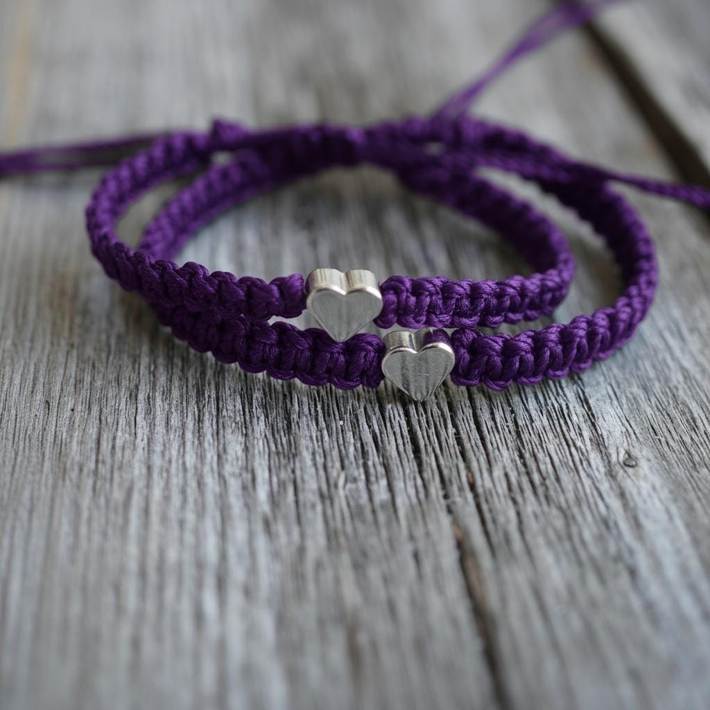 Two purple macrame bracelets with silver heart charms. The bracelets are knotted and have a braided appearance. The background is a weathered wooden surface.