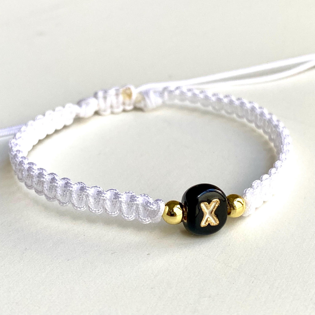 Handmade white macrame bracelet with a black ceramic letter bead and gold accents. The bracelet is adjustable with a sliding knot closure.