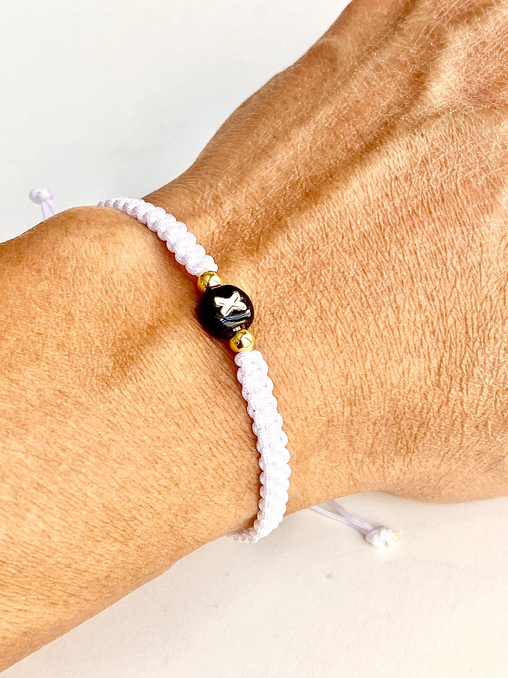 Handmade white macrame bracelet with a black ceramic letter bead and gold accents. The bracelet is adjustable with a sliding knot closure.