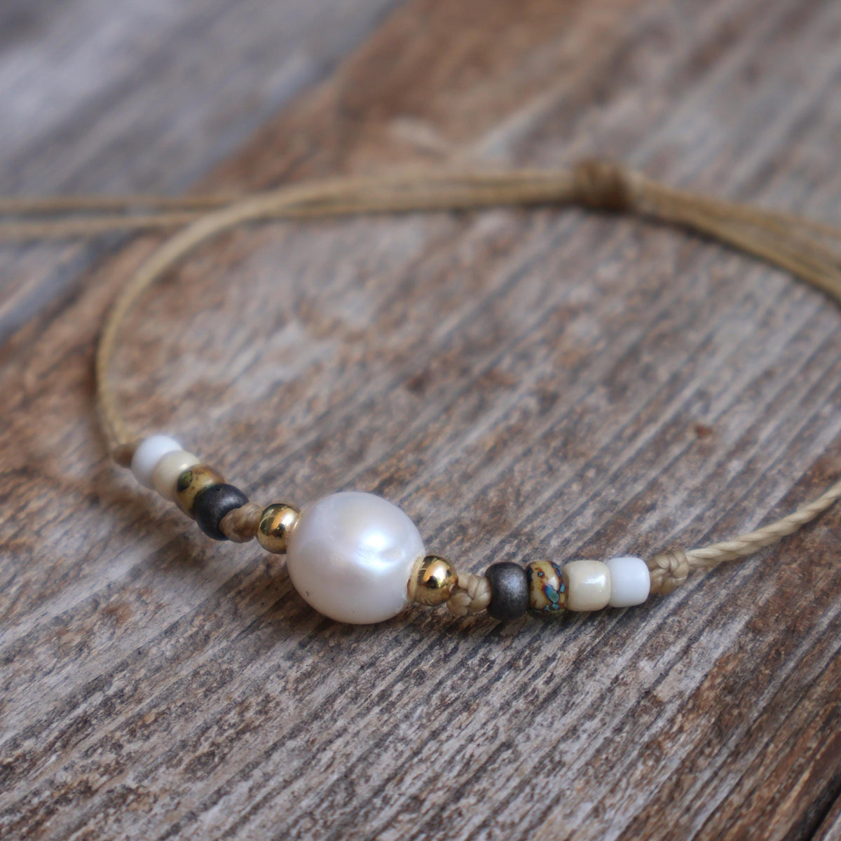 Boho pearl and beaded bracelet on tan waxed cord, rustic wood background.