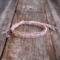 Blush pink macrame woven bracelet or anklet with adjustable slide-knot closure, laid on a rustic wooden background