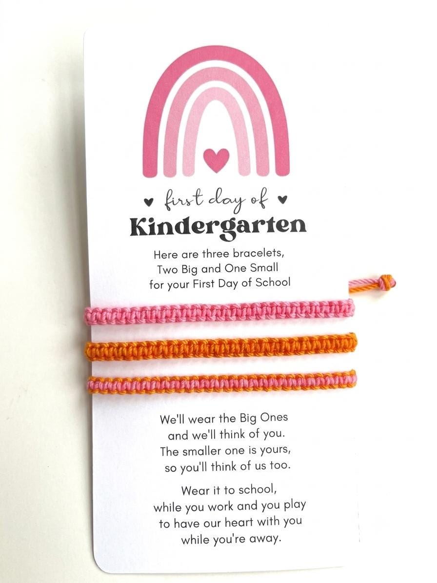 May include: Three woven bracelets in pink and orange attached to a white card featuring a pink rainbow graphic and the text: first day of Kindergarten. The card includes a poem about wearing the bracelets to school to stay connected.