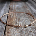 Minimalist gold waxed cord choker necklace with 6mm gold bead and adjustable knot closure, displayed on a wood background