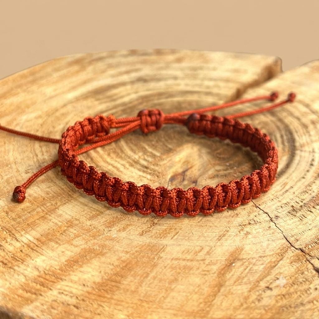 Rust colored macrame braided bracelet made from 1.5mm nylon cord with adjustable sliding knot, displayed on wood slice background"