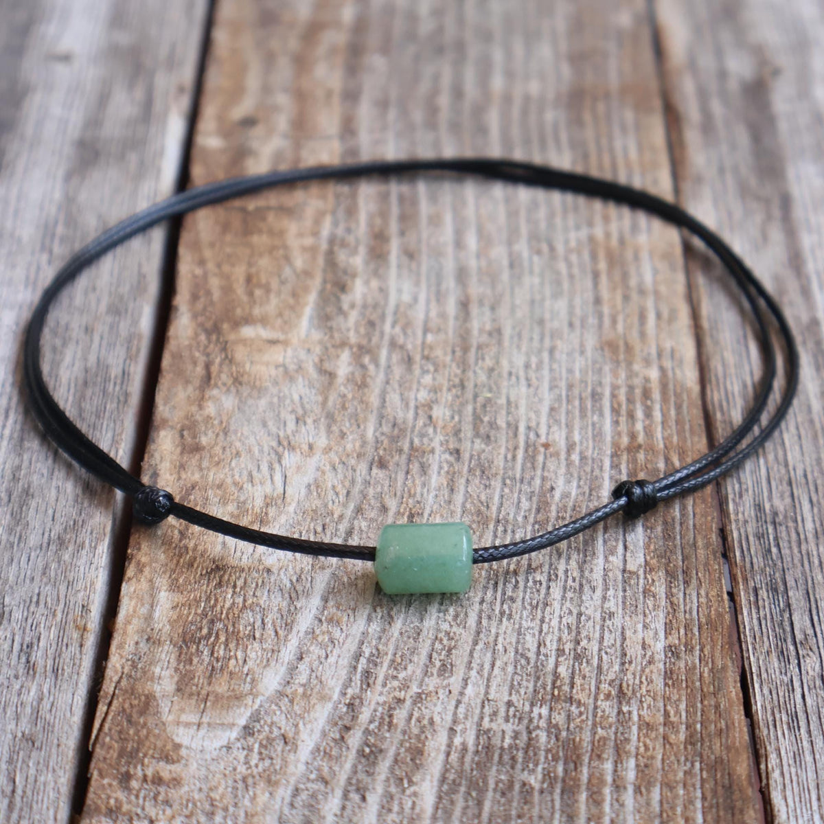 Green aventurine stone bead choker on black waxed cord with adjustable slide-knot closure, laid on a rustic wooden background.