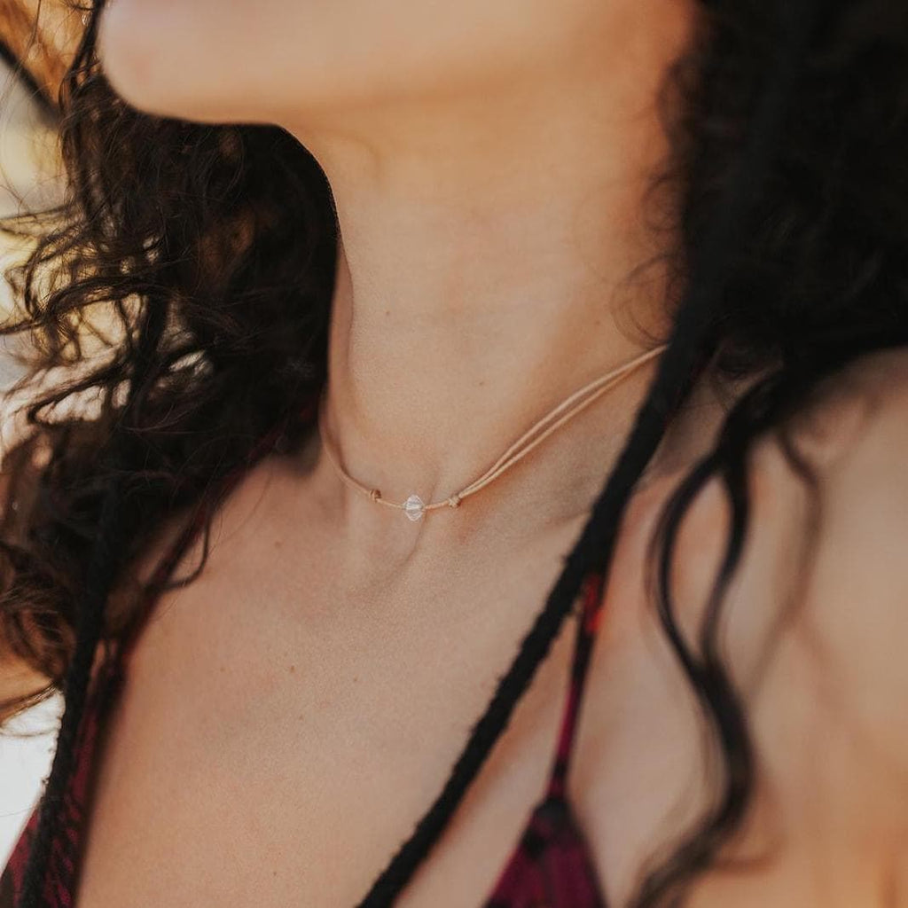 Swarovski crystal bicone bead choker on a tan cord necklace, worn layered on a woman's neck at the beach.