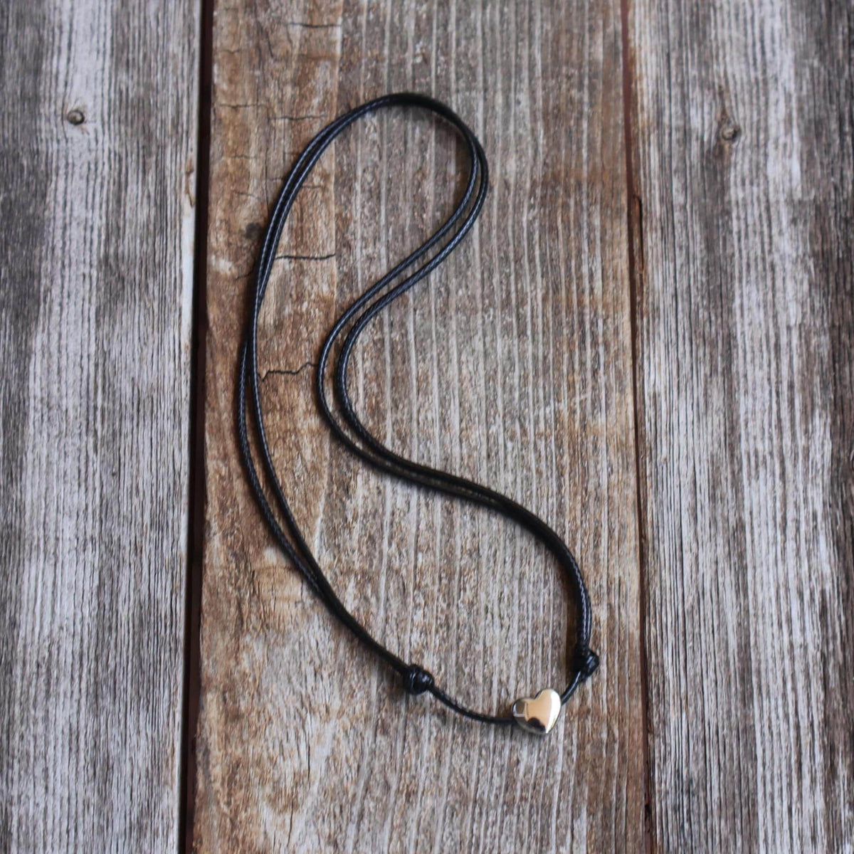 Sterling silver heart necklace with adjustable black cord, displayed on rustic wood background