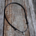 Swarovski birthstone crystal charm pendant on a black waxed cord necklace with adjustable slide-knot closure, laid on a rustic wooden background