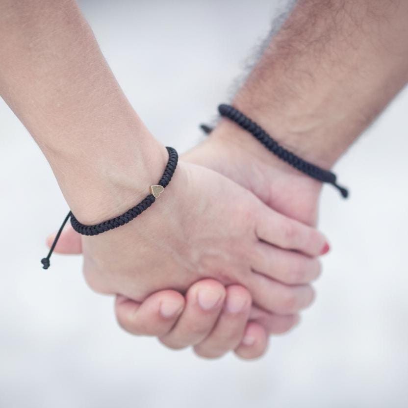 Handmade black braided couples bracelet set with heart detail, worn by man and woman holding hands