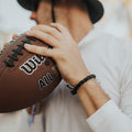 May include: A brown leather braided bracelet with a black adjustable clasp. The bracelet is worn on a person's wrist.