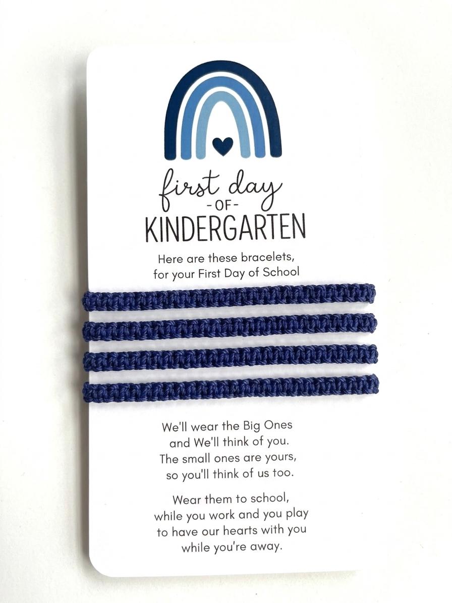 May include: Four dark blue woven cord bracelets attached to a white display card. The card features a blue rainbow graphic, a heart, and the text: first day OF KINDERGARTEN. It includes a poem about wearing bracelets to school to stay connected.