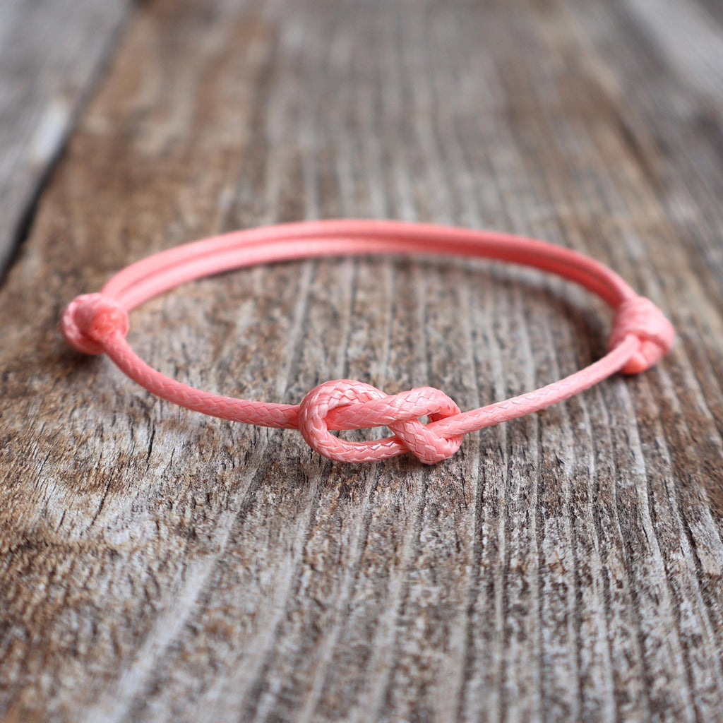 Salmon infinity knot bracelet/anklet with adjustable closure, available in multiple colors, displayed on wood background"