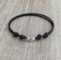 Silver crescent moon charm bracelet on black waxed cord, adjustable knot closure displayed on wood background