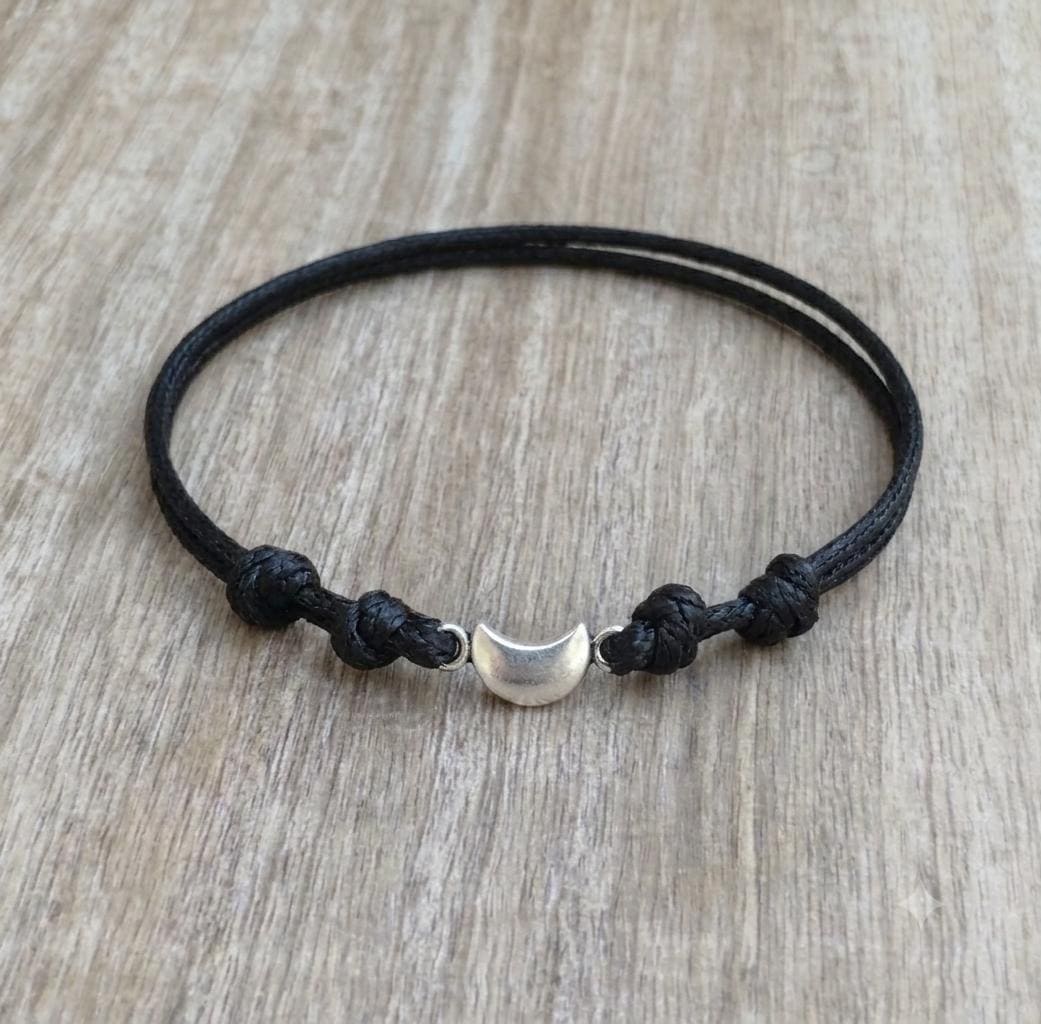 Silver crescent moon charm bracelet on black waxed cord, adjustable knot closure displayed on wood background