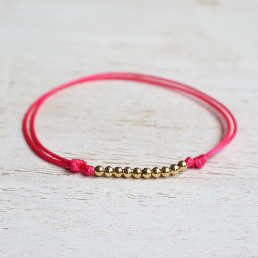 A pink neon string anklet bracelet with a small gold beads