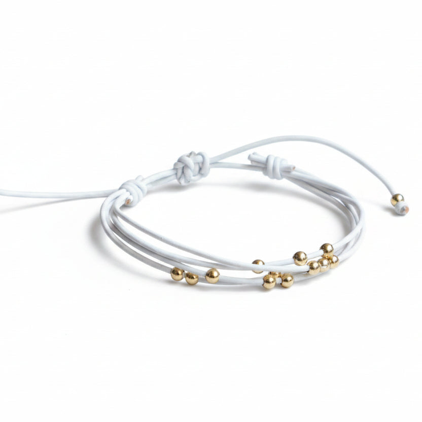 White leather wrap bracelet with gold beads on rustic wood background