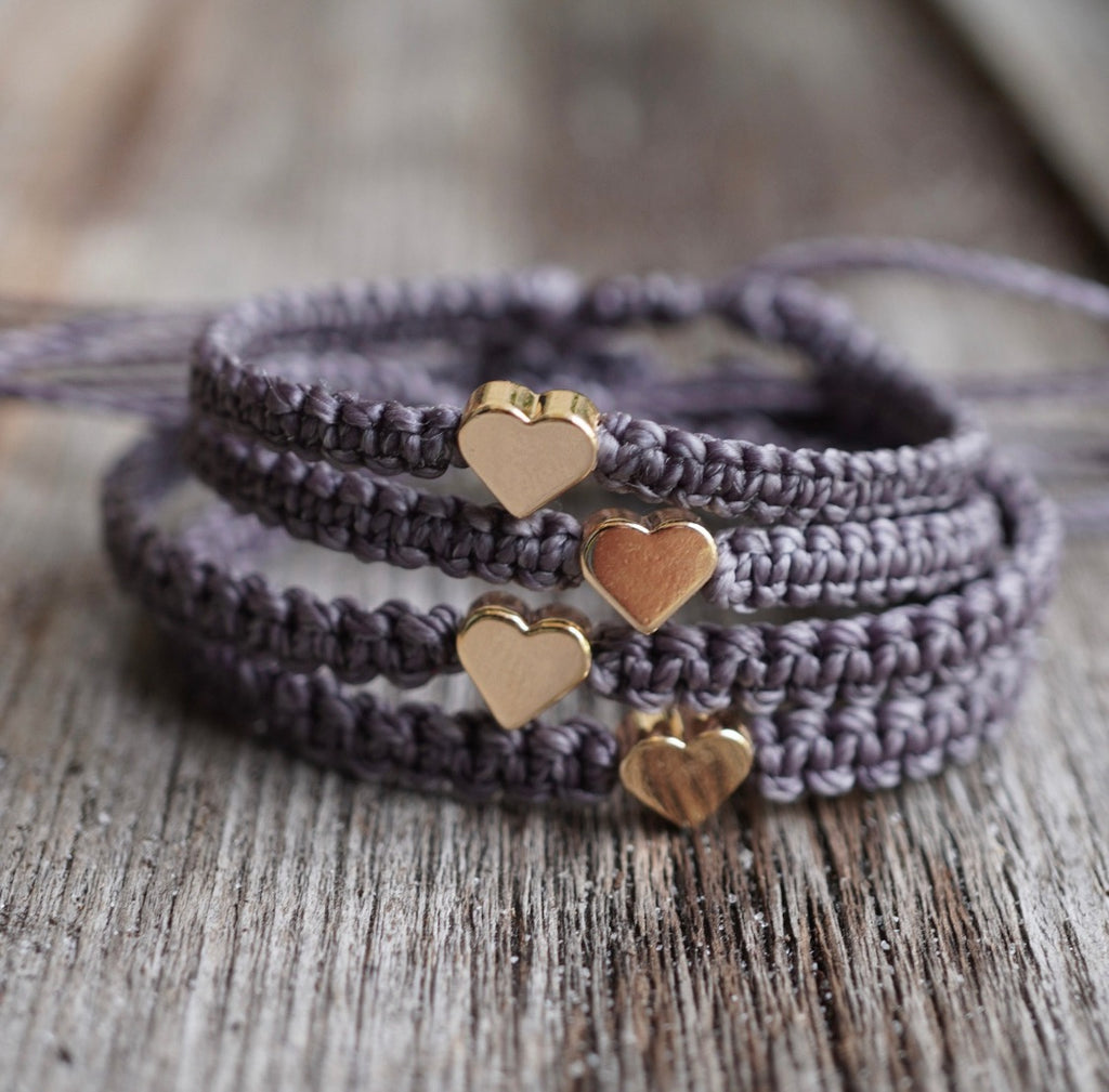 Set of matching family bracelets in gray macrame cord with gold heart charms, handmade adjustable design, displayed on rustic wood background.