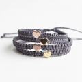 Gray braided bracelet with gold heart-shaped charms on a white background