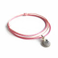 A pink freshwater pearl anklet with a silver-colored bead, displayed on a wooden surface with a branded text overlay.