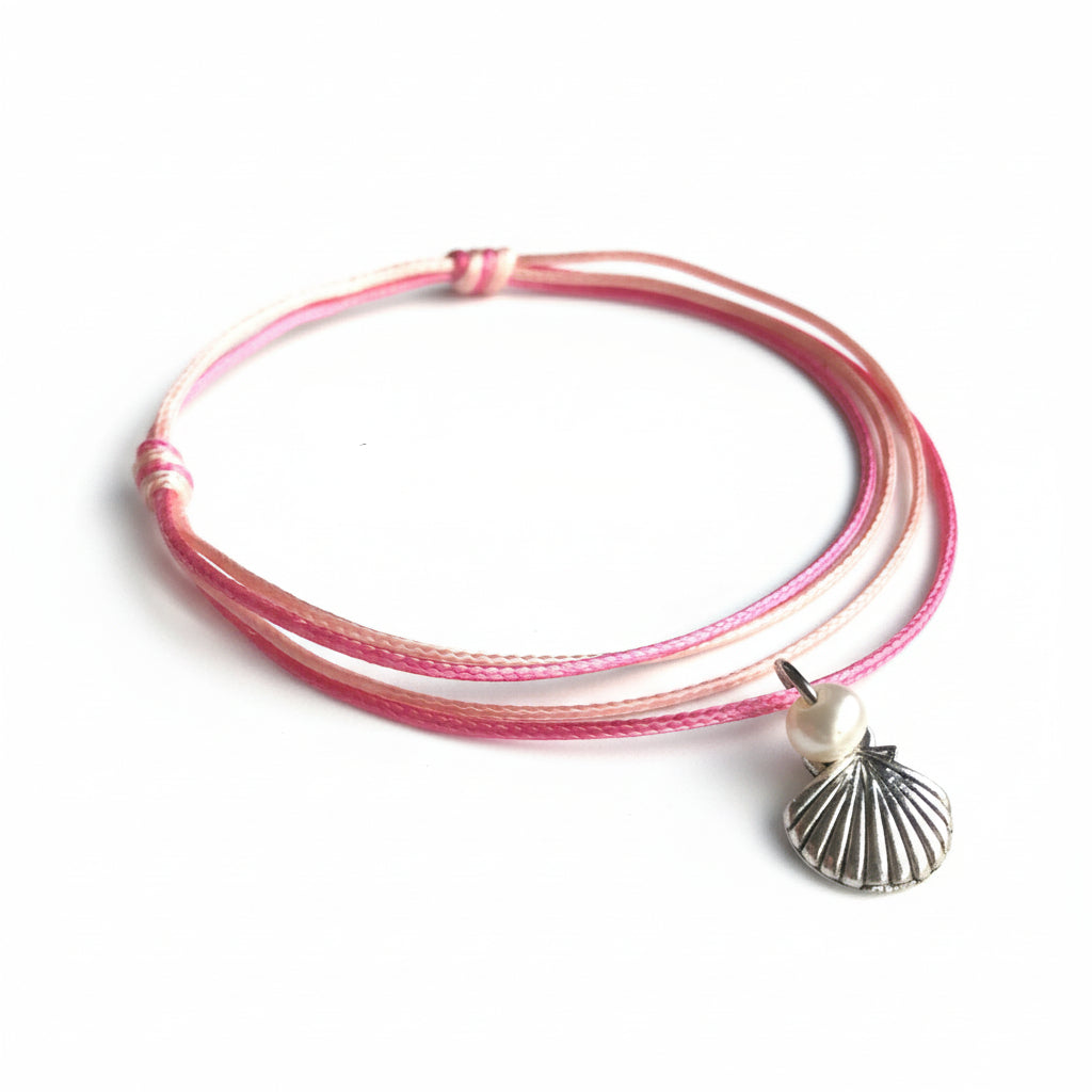 A pink freshwater pearl anklet with a silver-colored bead, displayed on a wooden surface with a branded text overlay.