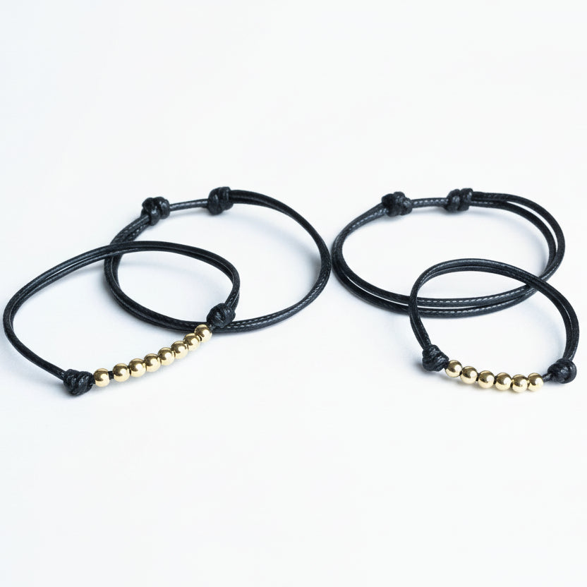 Two black braided bracelets with gold beads on a white background