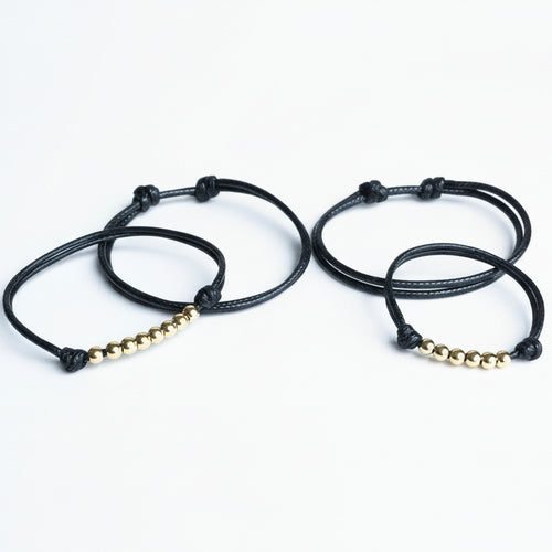 Two black braided bracelets with gold beads on a white background